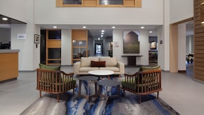A spacious lobby with a high ceiling, a central seating area with a sofa and chairs, and a reception desk to the left. - Fairfield Inn & Suites by Marriott Charleston (South Charleston)