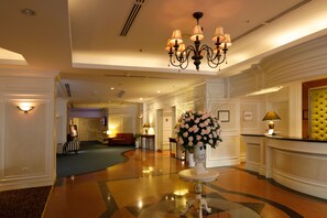 Een hotel lobby met een receptiebalie, een kroonluchter, een bloemenvaas en een zithoek.