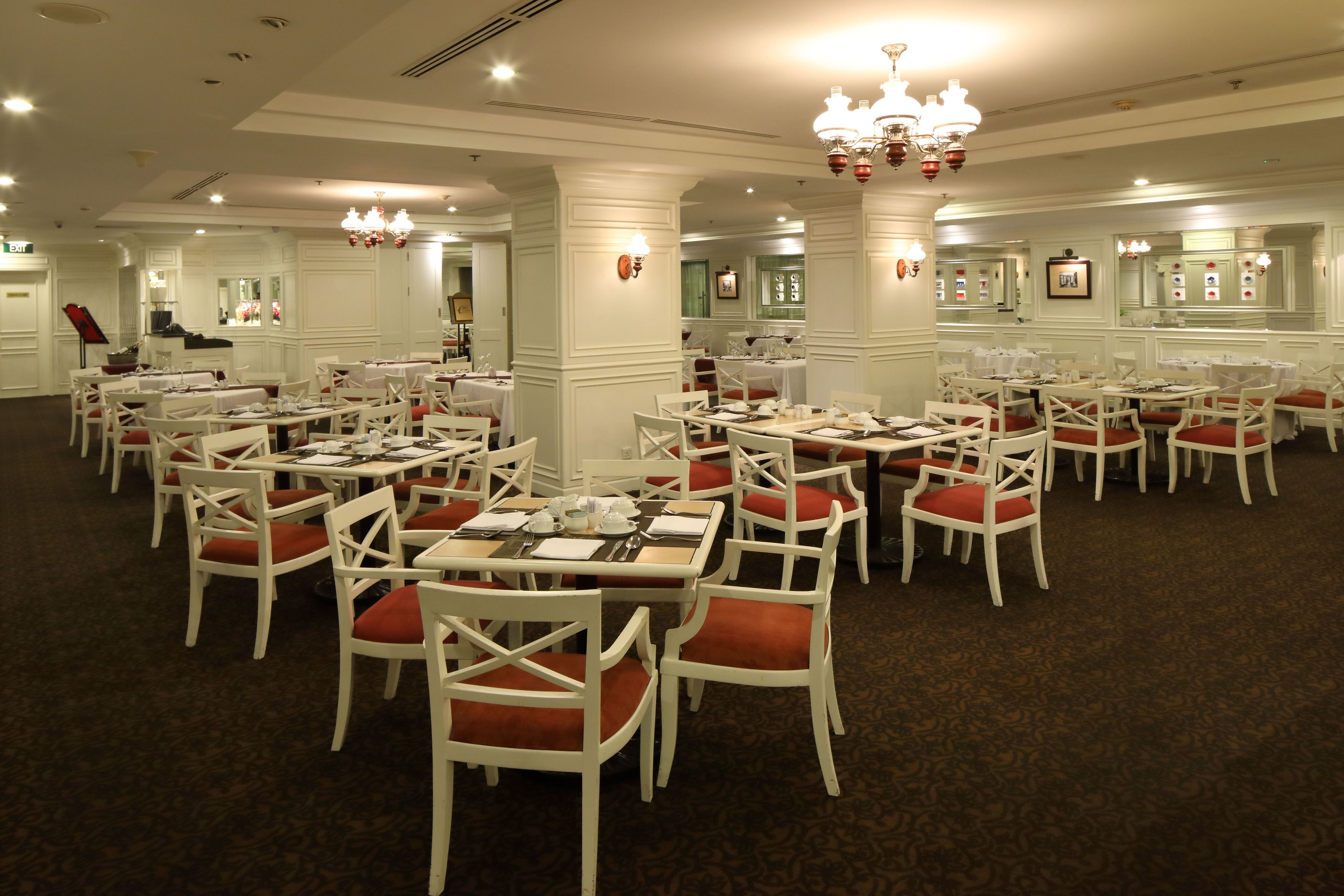 Un comedor formal con mesas y sillas blancas, asientos acolchados rojos y un candelabro.