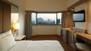 A hotel room with a large bed, a desk, a chair, a TV, and a window with a city view. - Sunway Hotel Hanoi (Hanoi)