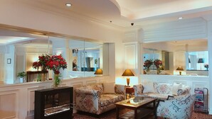A spacious living room with a large mirror, floral-patterned sofas, a glass coffee table, and a fireplace. - Sunway Hotel Hanoi (Hanoi)