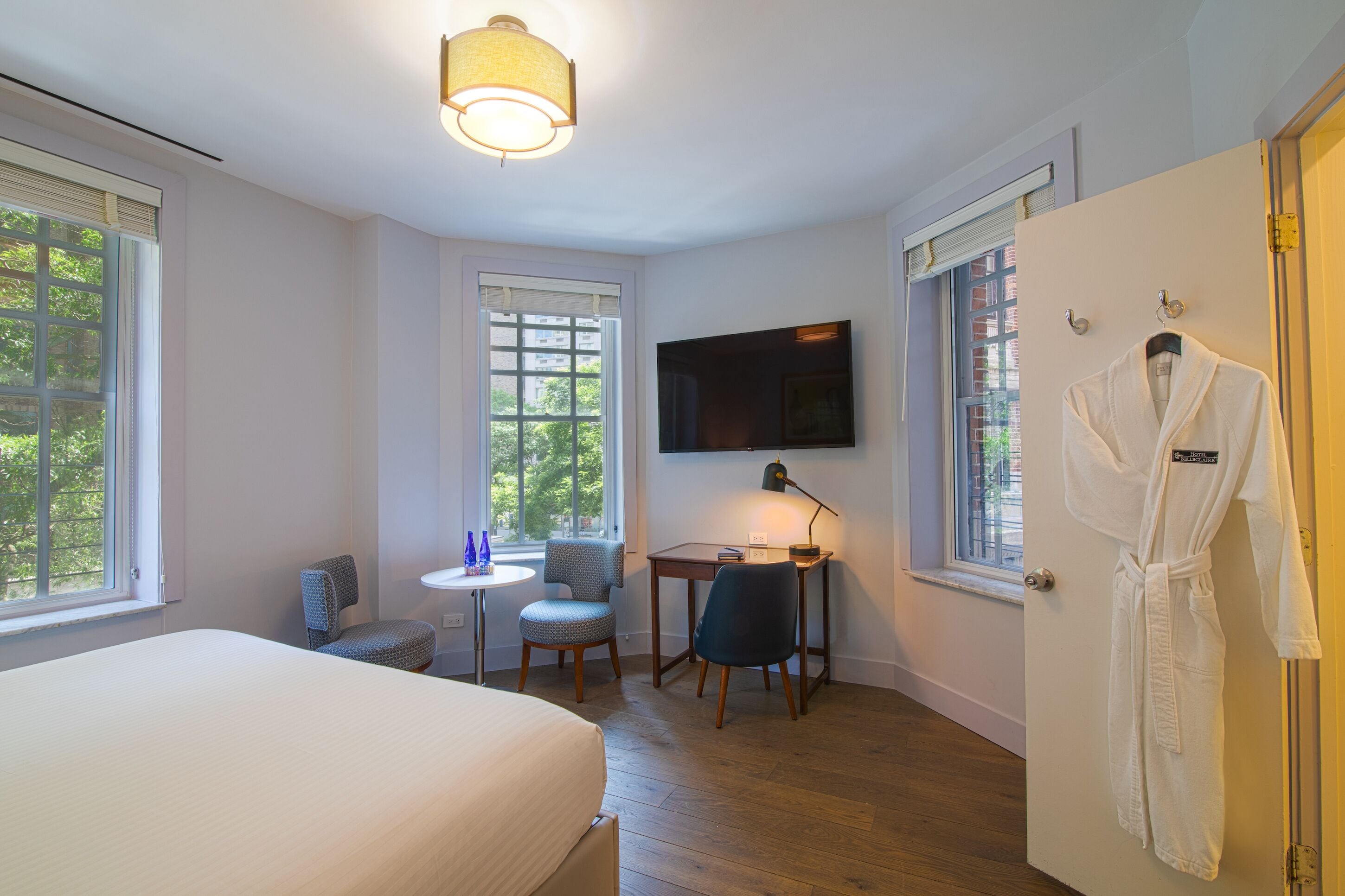 Een hotelkamer met een bed, een bureau met stoel, een aan de muur bevestigde televisie en een badjas hangend aan de deur.