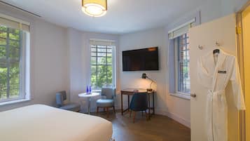 Een hotelkamer met een bed, een bureau met stoel, een aan de muur bevestigde televisie en een badjas hangend aan de deur.