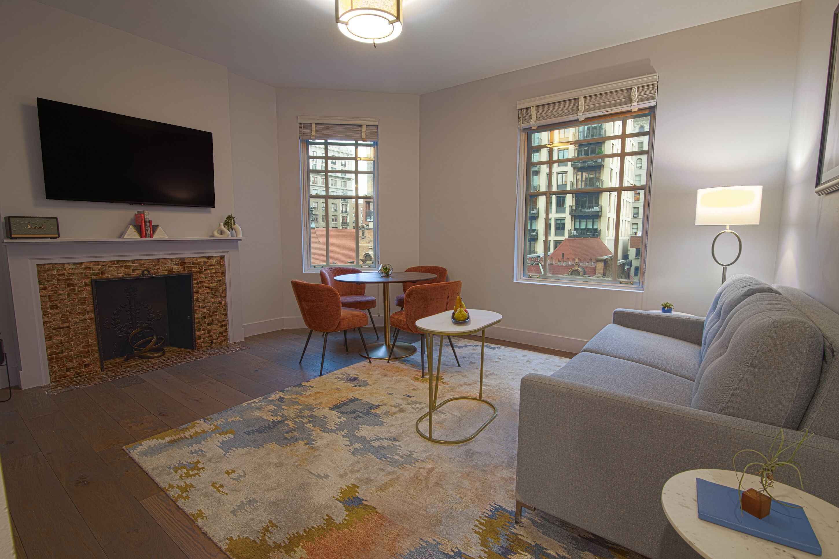 Una sala de estar con chimenea, un televisor de pantalla plana, un sofá, una mesa de comedor con sillas y ventanas grandes.