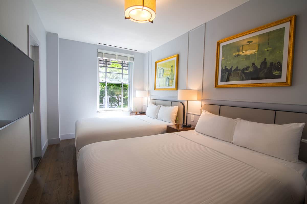 Habitación de hotel con dos camas, un televisor de pantalla plana, un ventanal con vistas a la vegetación y dos cuadros en la pared.
