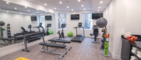 Un gimnasio moderno con varios equipos de ejercicio, incluyendo cintas de correr, mancuernas y pelotas de ejercicio.