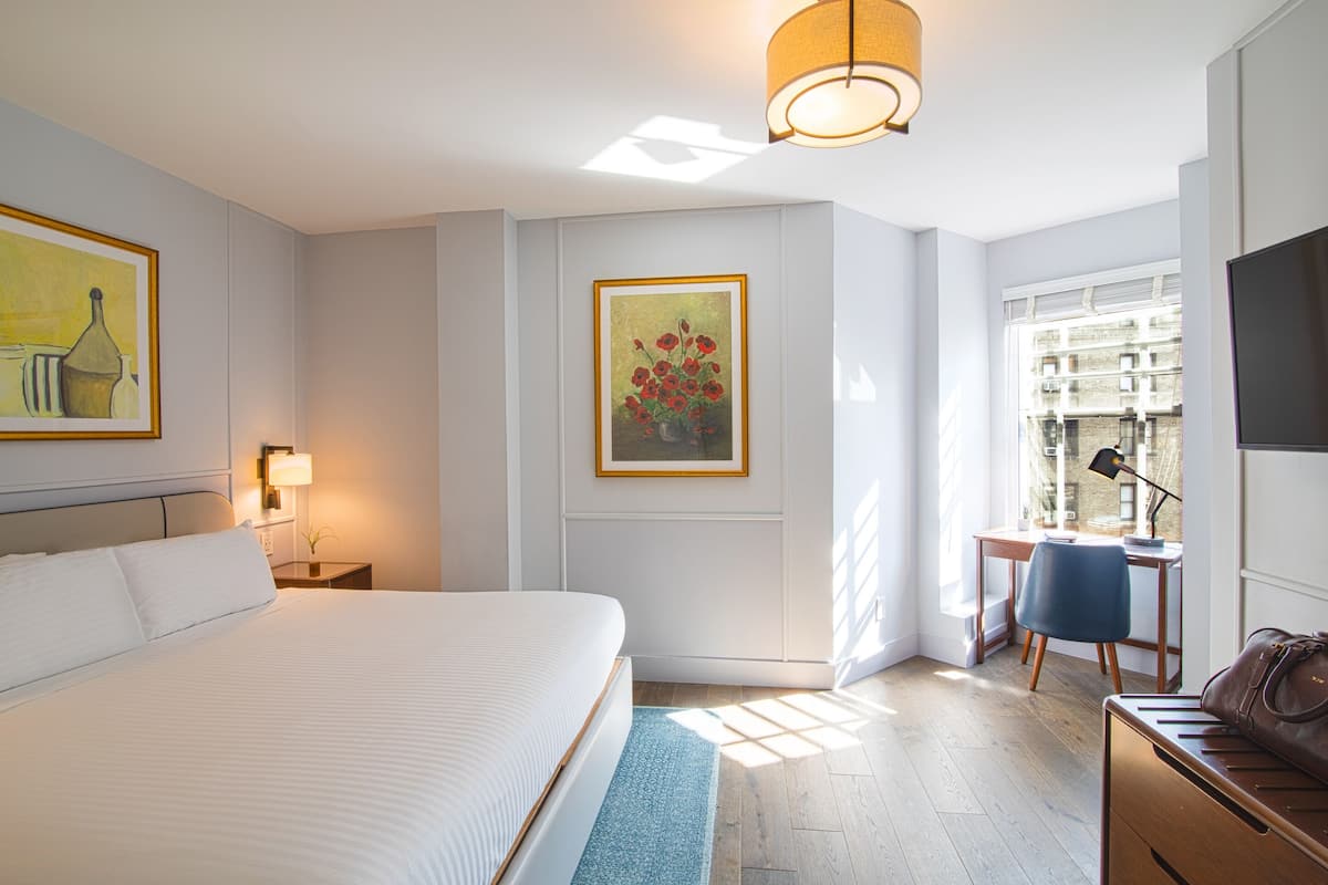 Habitación de hotel con una cama grande, un escritorio con silla, televisor y obras de arte en las paredes.