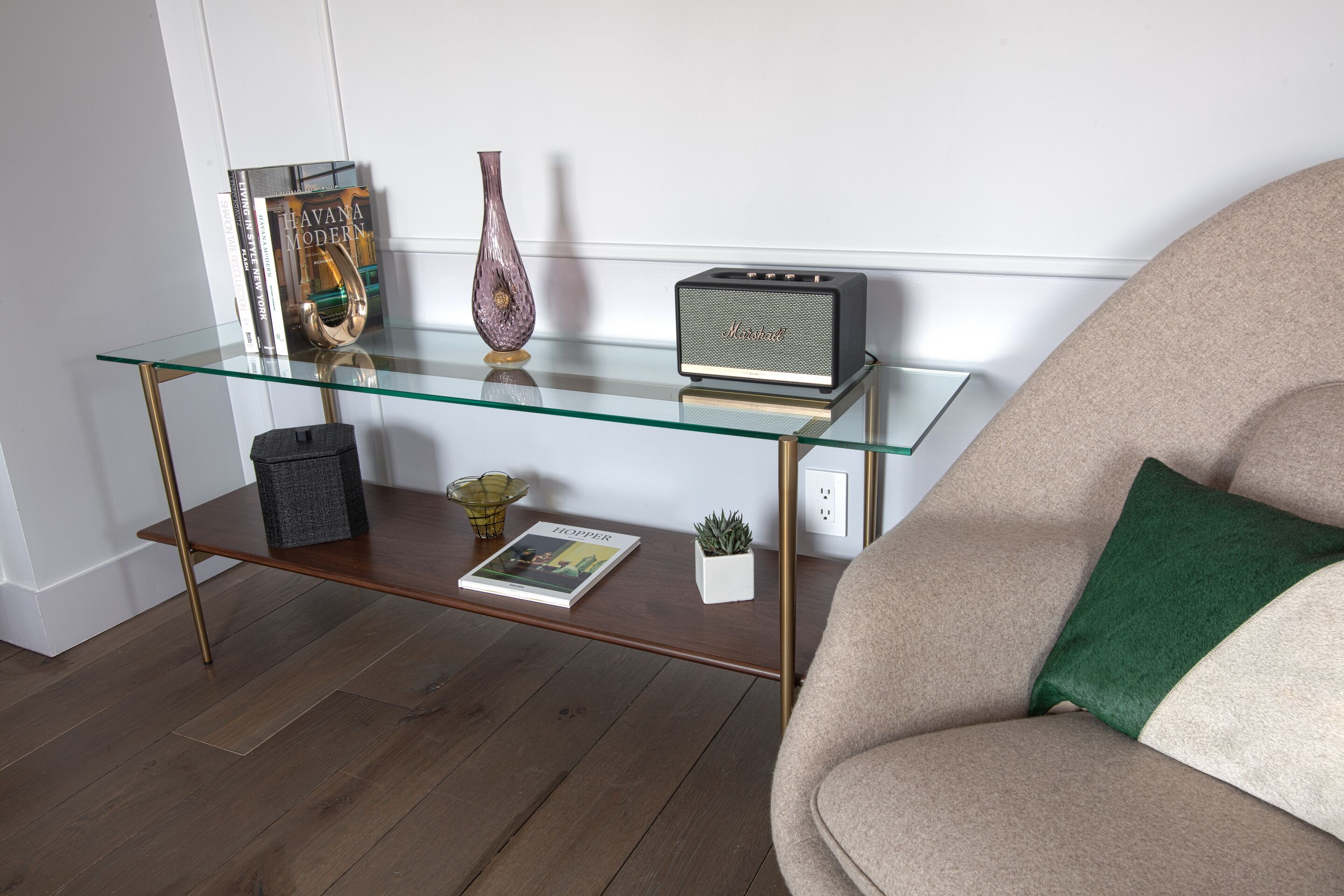 Una mesa de centro con cubierta de vidrio, libros, un florero, un altavoz y una pequeña planta.