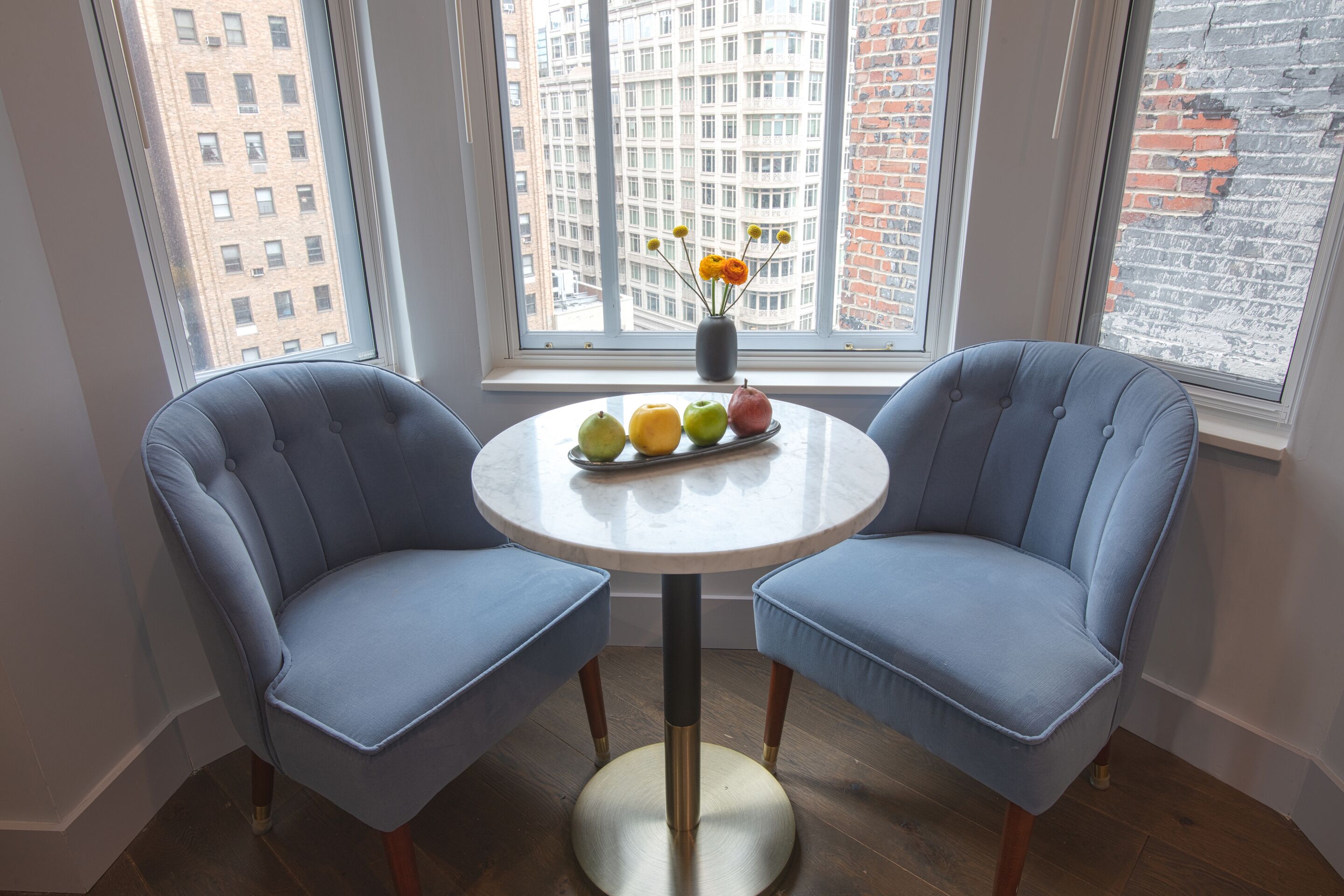 Un coin repas comprenant deux chaises bleues à revêtement rembourré, une table ronde et un vase avec des fleurs.