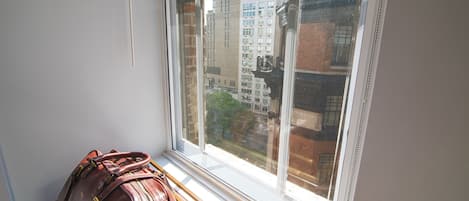 A window with a view of buildings and a brown leather bag on a bench.