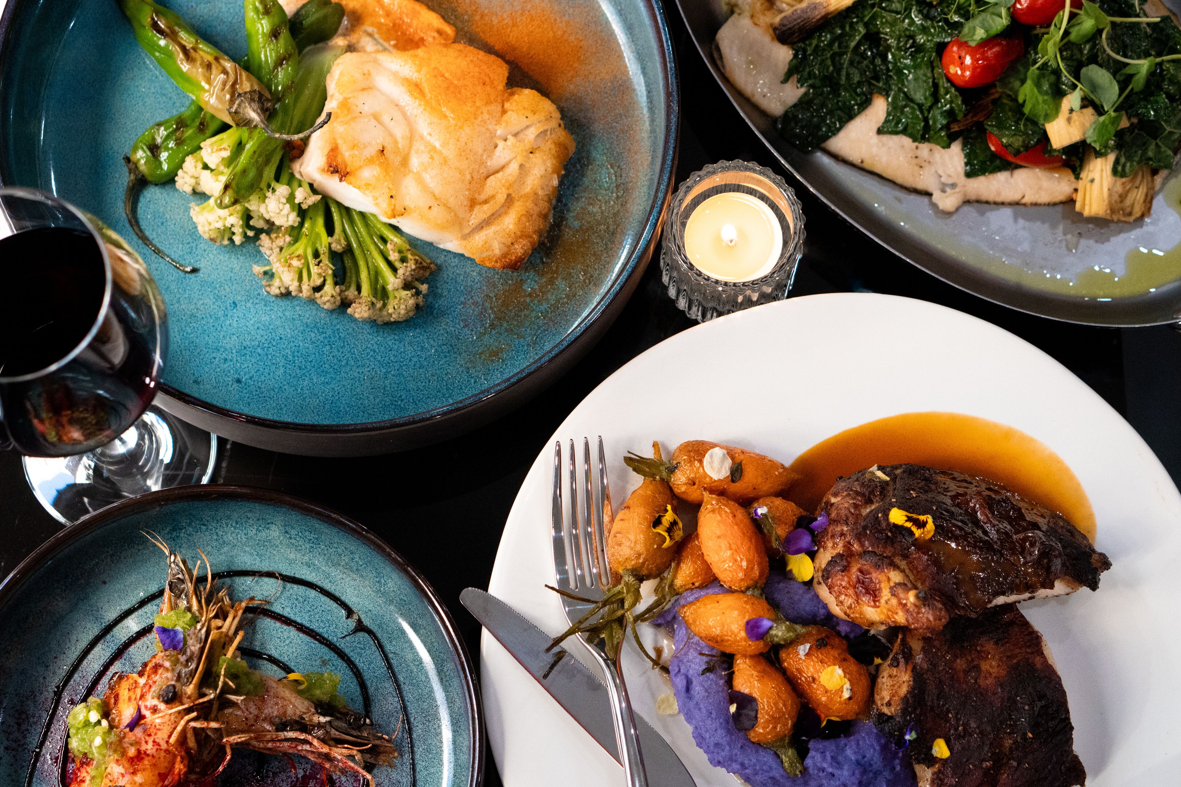 A table with various dishes, including seafood, vegetables, and a steak, suggesting a fine dining experience.