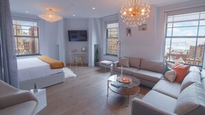A modern living room with a sofa, a glass coffee table, and a bed with a white headboard.