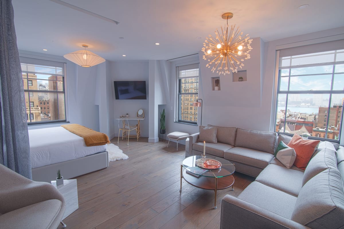 Una sala moderna con sofá, una mesa de centro de vidrio y una cama con cabecera blanca.