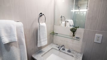 A modern bathroom with a marble sink, two towel rings, a glass shelf with a vase, and a large mirror.