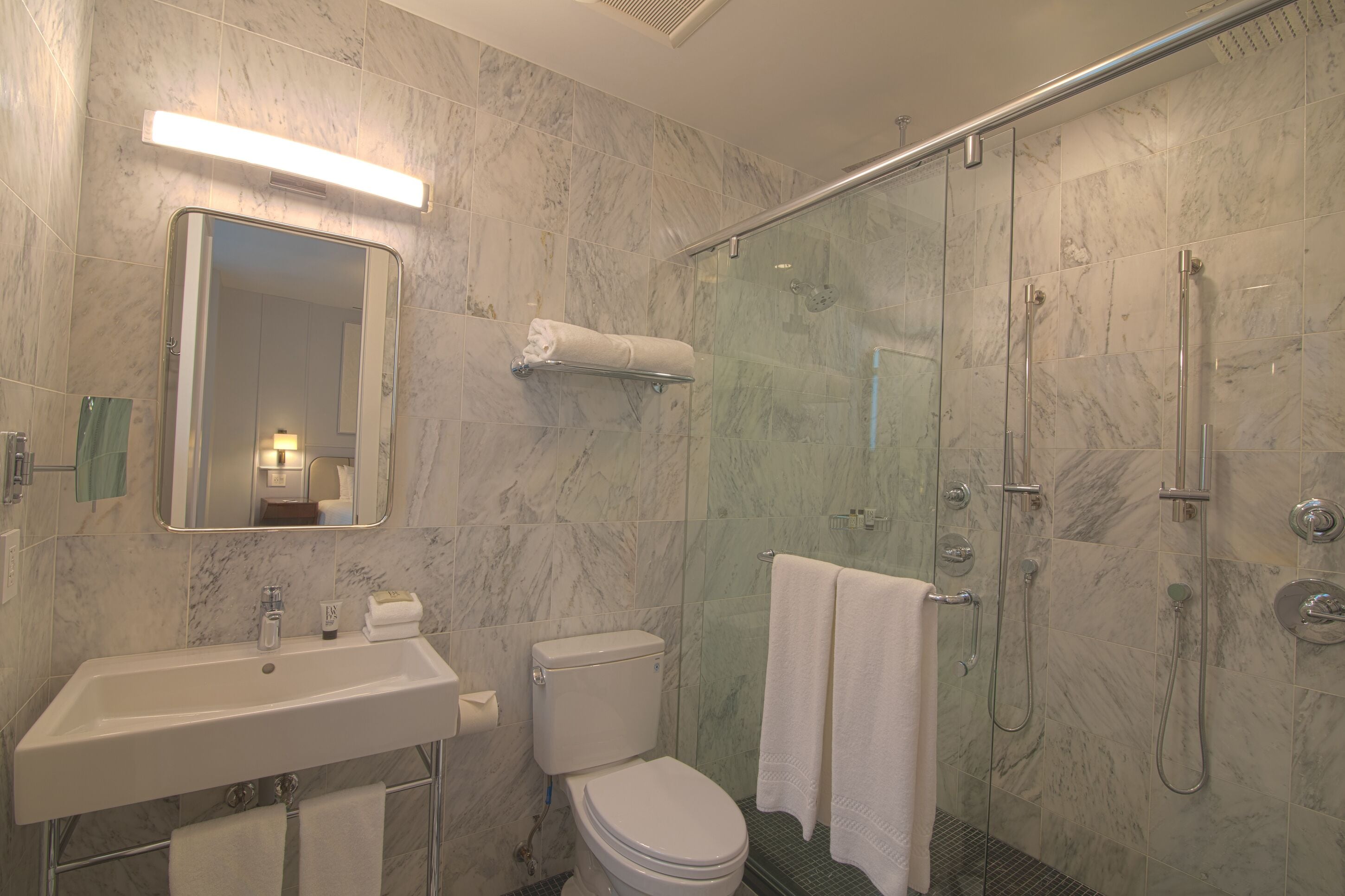 Un baño con lavamanos, inodoro y cabina de ducha con mampara de vidrio.