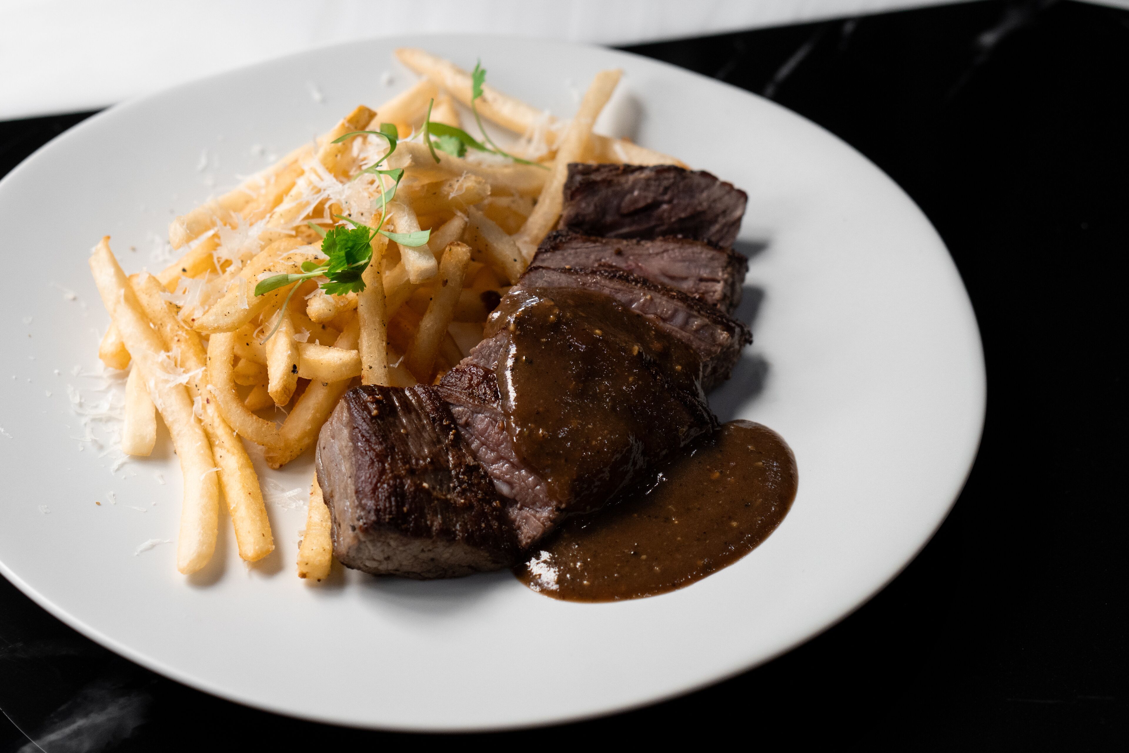 Un plato con carne en rodajas y papas fritas.