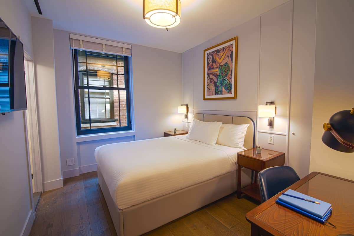 Habitación de hotel con una cama grande, lámparas de noche, un escritorio con silla y una ventana con persianas.