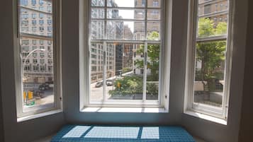 A corner room with a large window overlooking a city street, a bench, and a view of buildings.