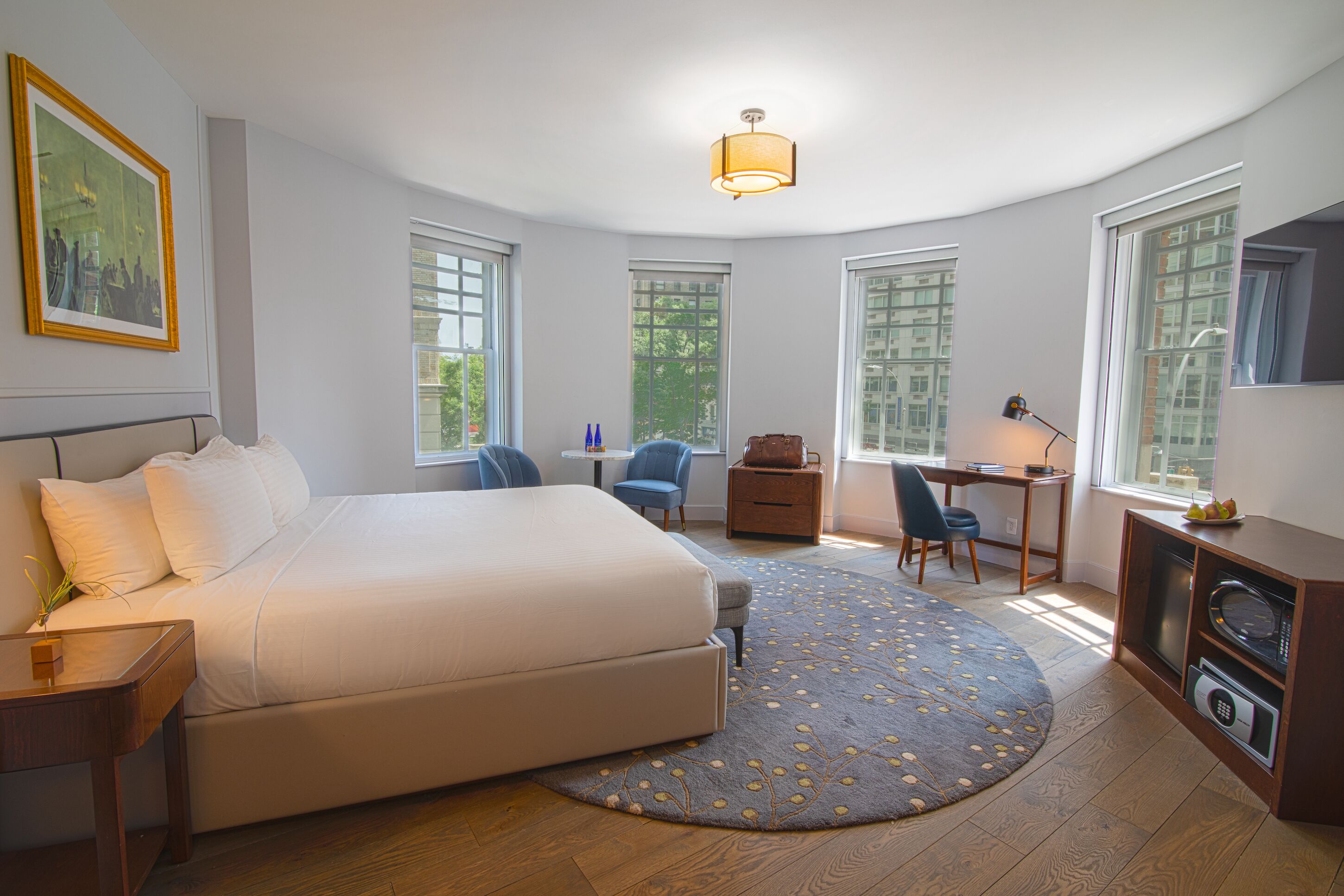 Ein Hotelzimmer mit einem großen Bett, einem Schreibtisch, einem Stuhl, einem kleinen Tisch, einer Mikrowelle und einem Fernseher.