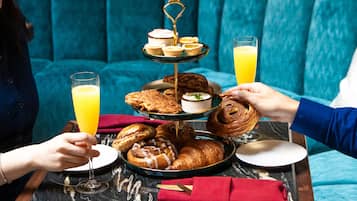 Una bandeja de desayuno con pasteles, un pastelero escalonado y vasos de zumo de naranja sobre una mesa de mármol.