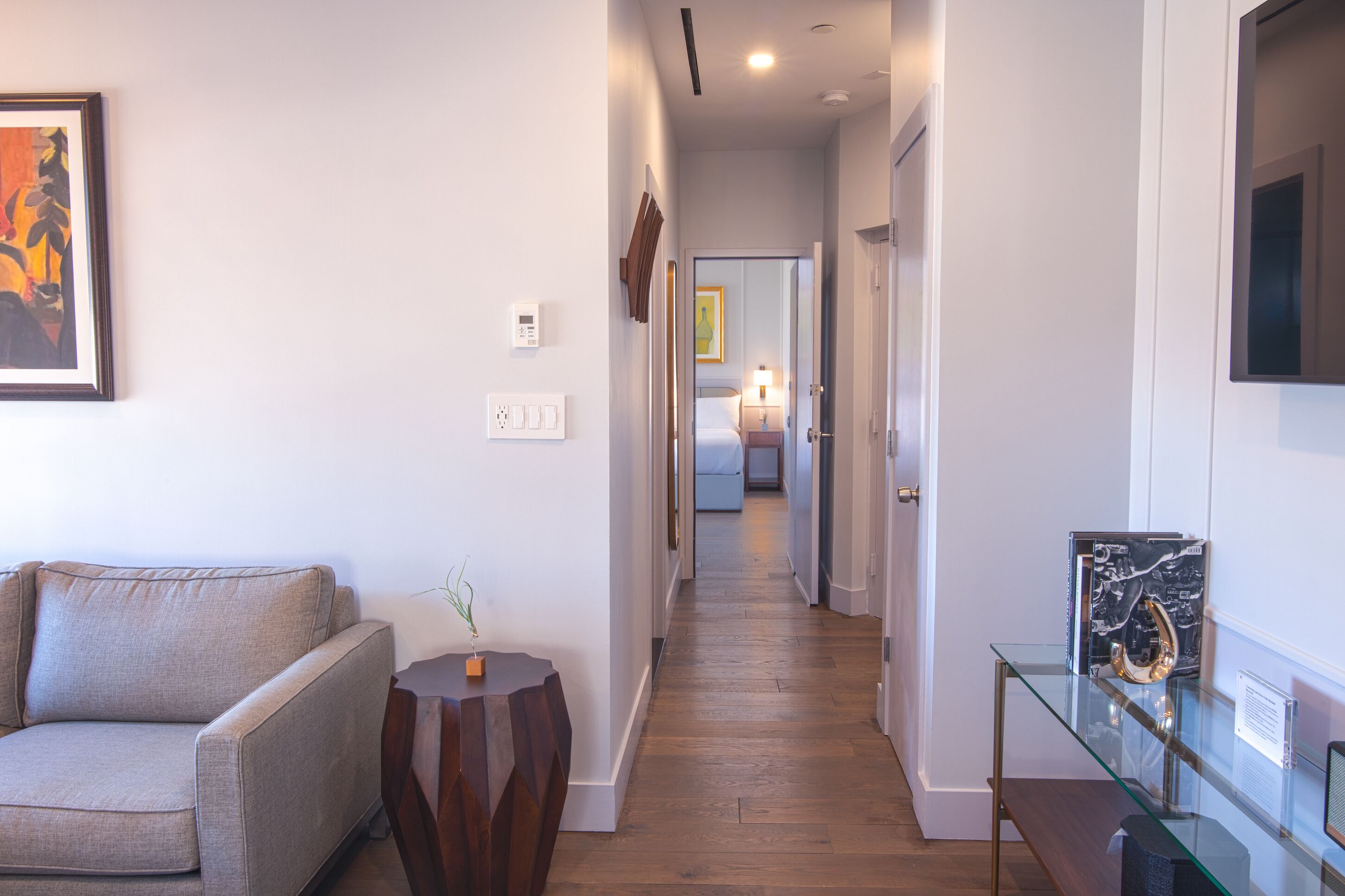 A hallway with a sofa, a small table with a plant, a glass display case with an object, and a door leading to another room.