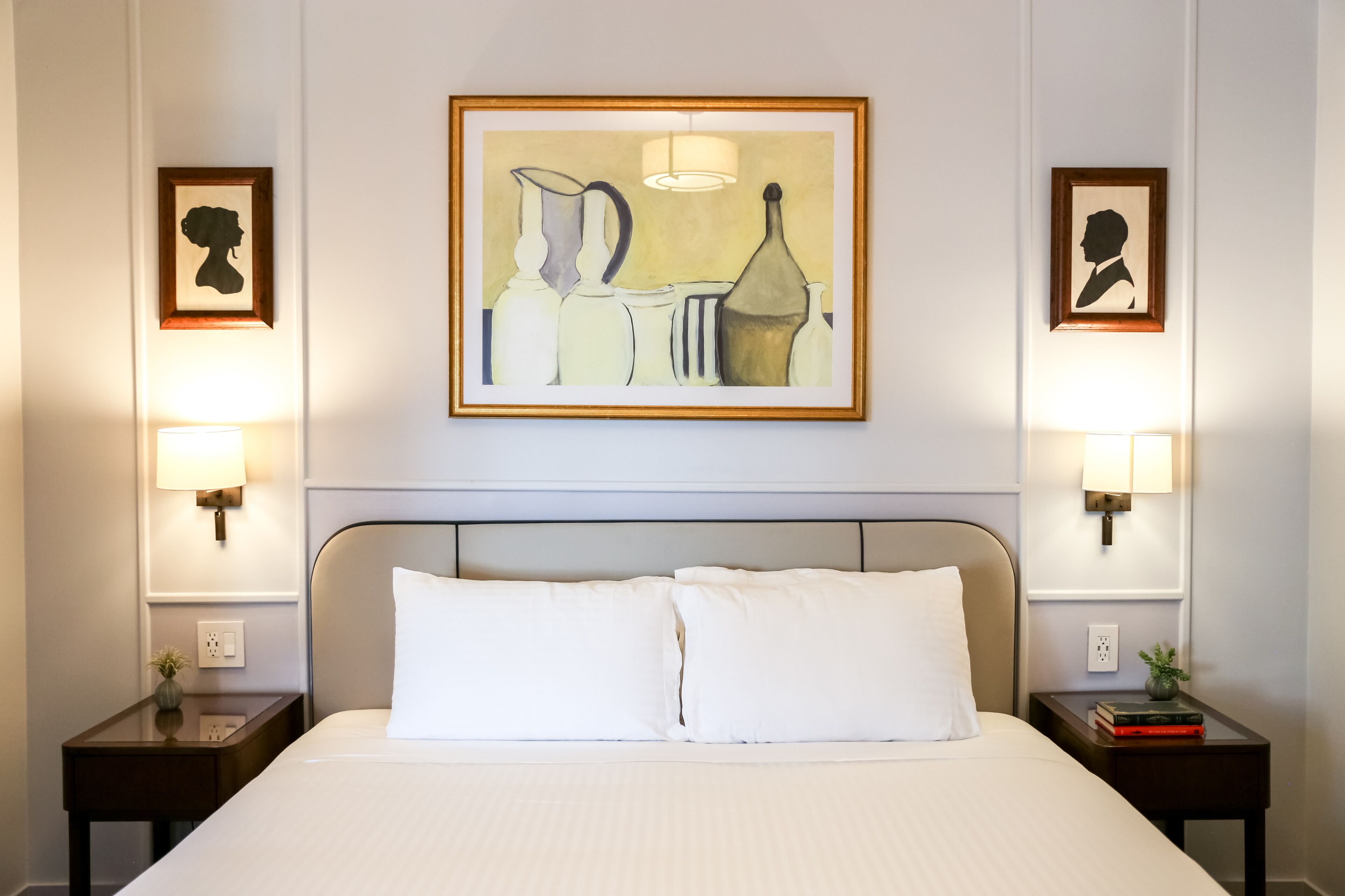 A hotel room with a large bed, two bedside tables with lamps, and two framed artworks on the walls.