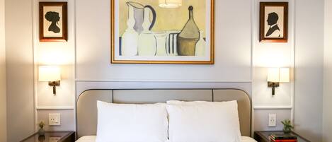 A hotel room with a large bed, two bedside tables with lamps, and two framed artworks on the walls.