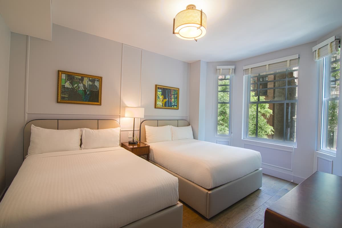 Habitación de hotel con dos camas, una mesa de comedor y ventanas amplias con vistas a zonas verdes.