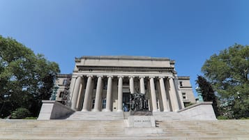 A grand building with classical architecture, featuring a prominent statue at the entrance and steps leading up to it.