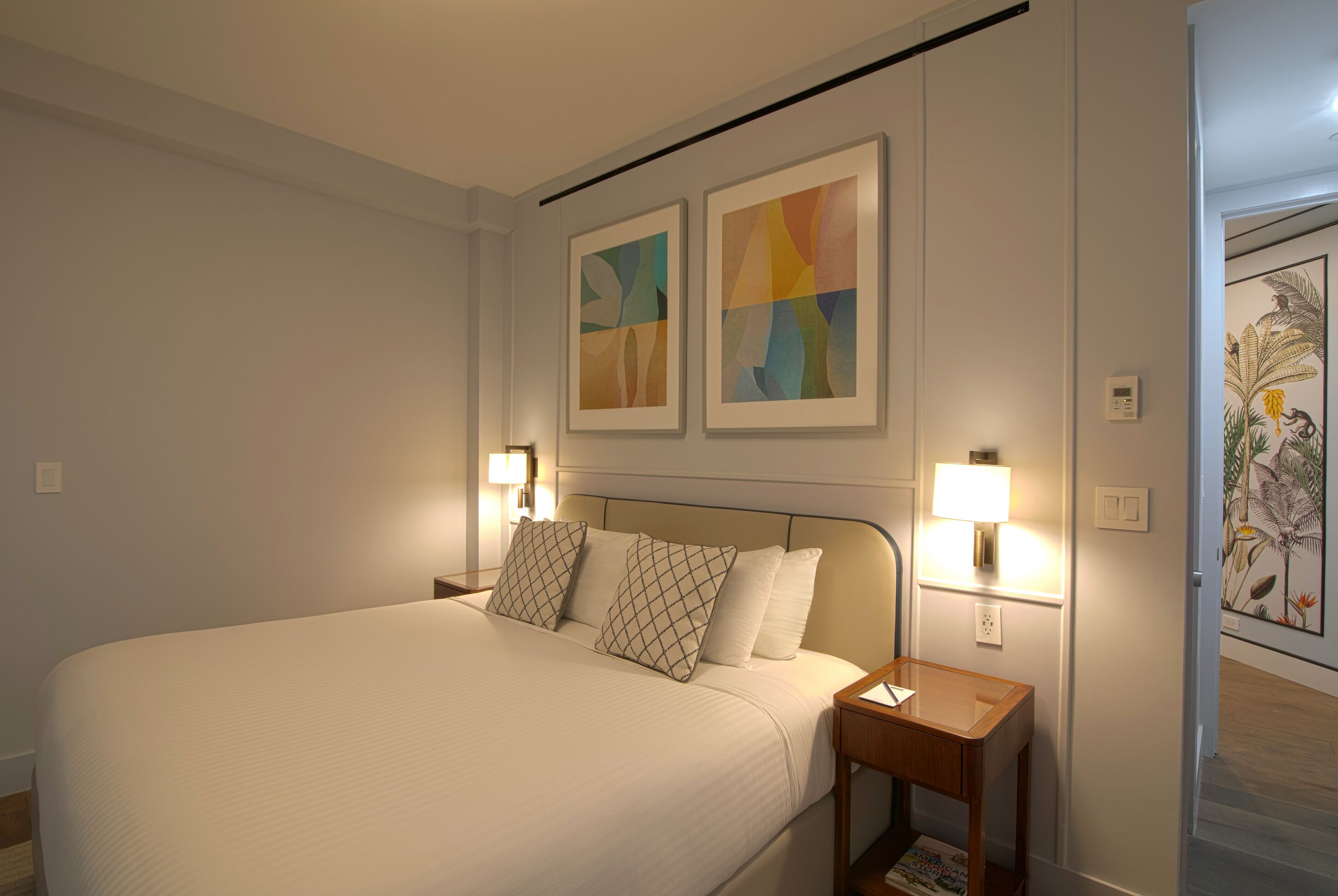 A hotel room with a large bed, two bedside lamps, and two abstract paintings on the wall.