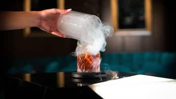 A hand pouring a clear liquid into a glass, creating a smoky effect.