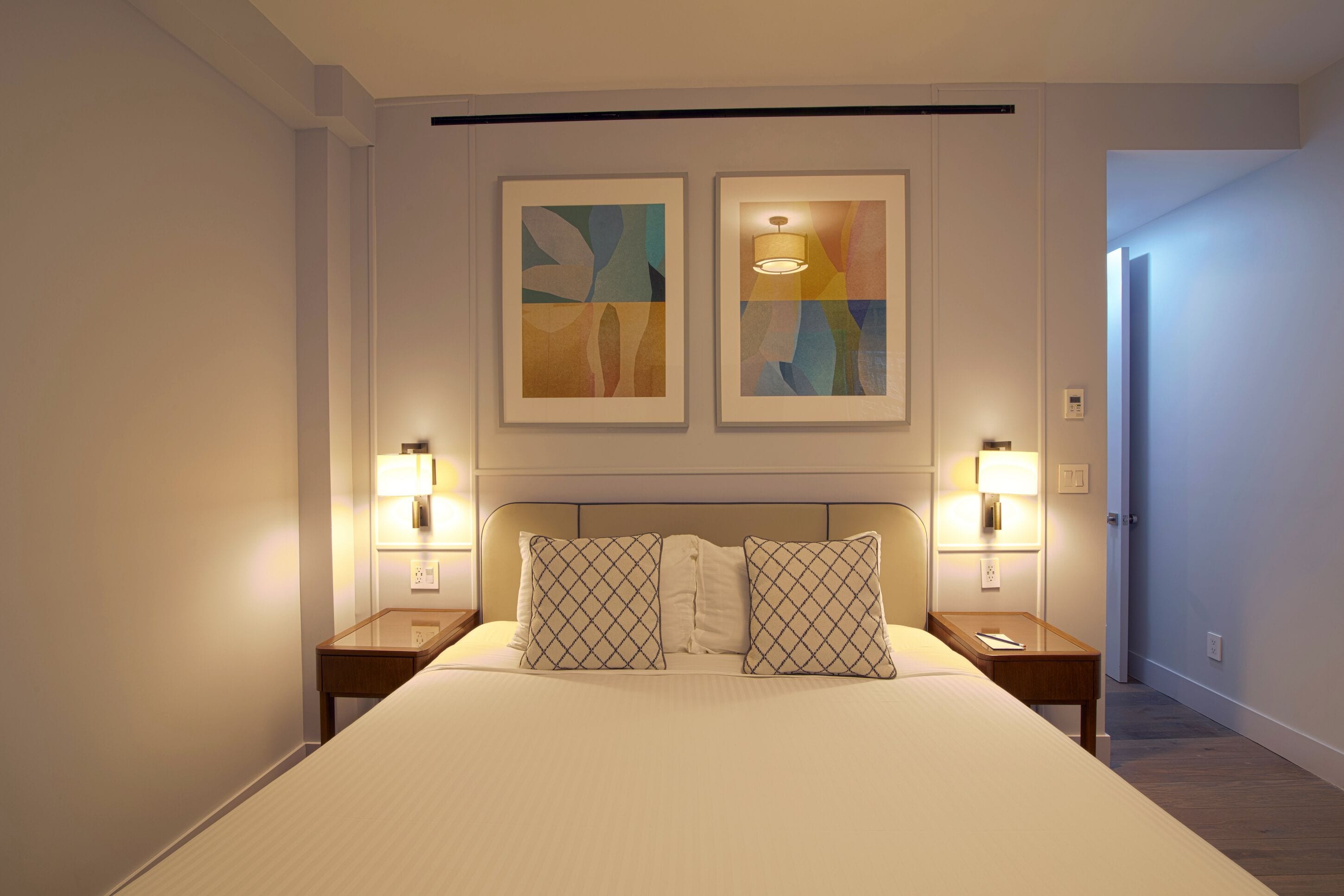 Una habitación de hotel con una cama grande, dos mesitas de noche con lámparas y arte abstracto en la pared.