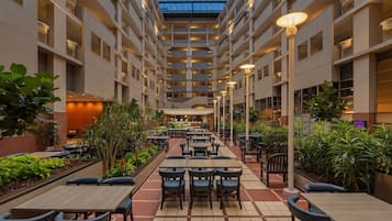 Ein mehrgeschossiges Atrium mit Esstischen und Stühlen, umgeben von Pflanzen und einer Glasdecke.