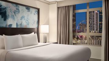 Een hotelkamer met een groot bed, een nachtkastje, een lamp, een schilderij en een raam met uitzicht over de stad.