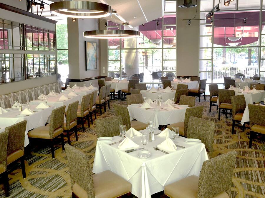 A restaurant with multiple tables set for dining, featuring white tablecloths and chairs.