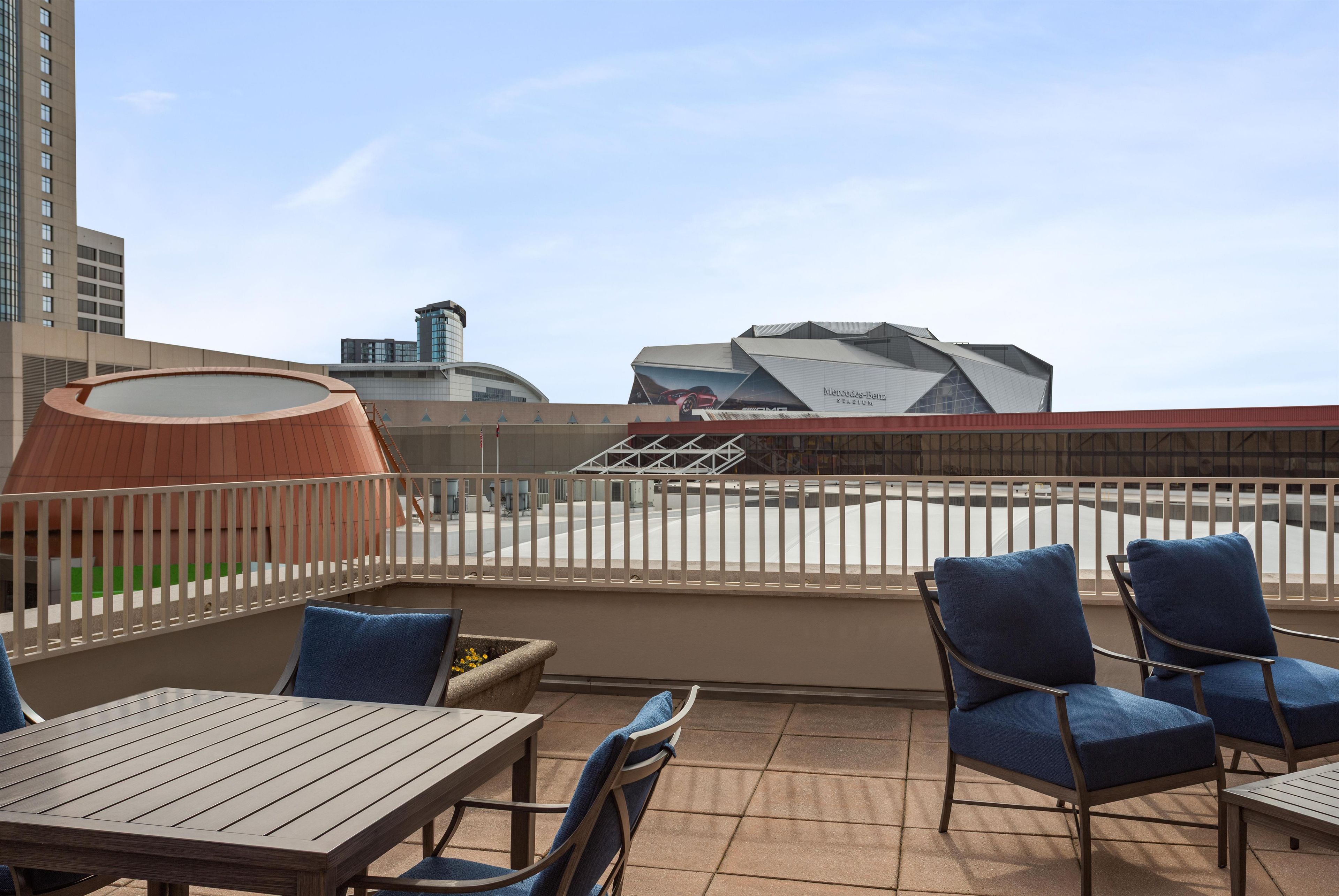 A rooftop terrace with a wooden table and chairs, a view of a modern building, and a railing.