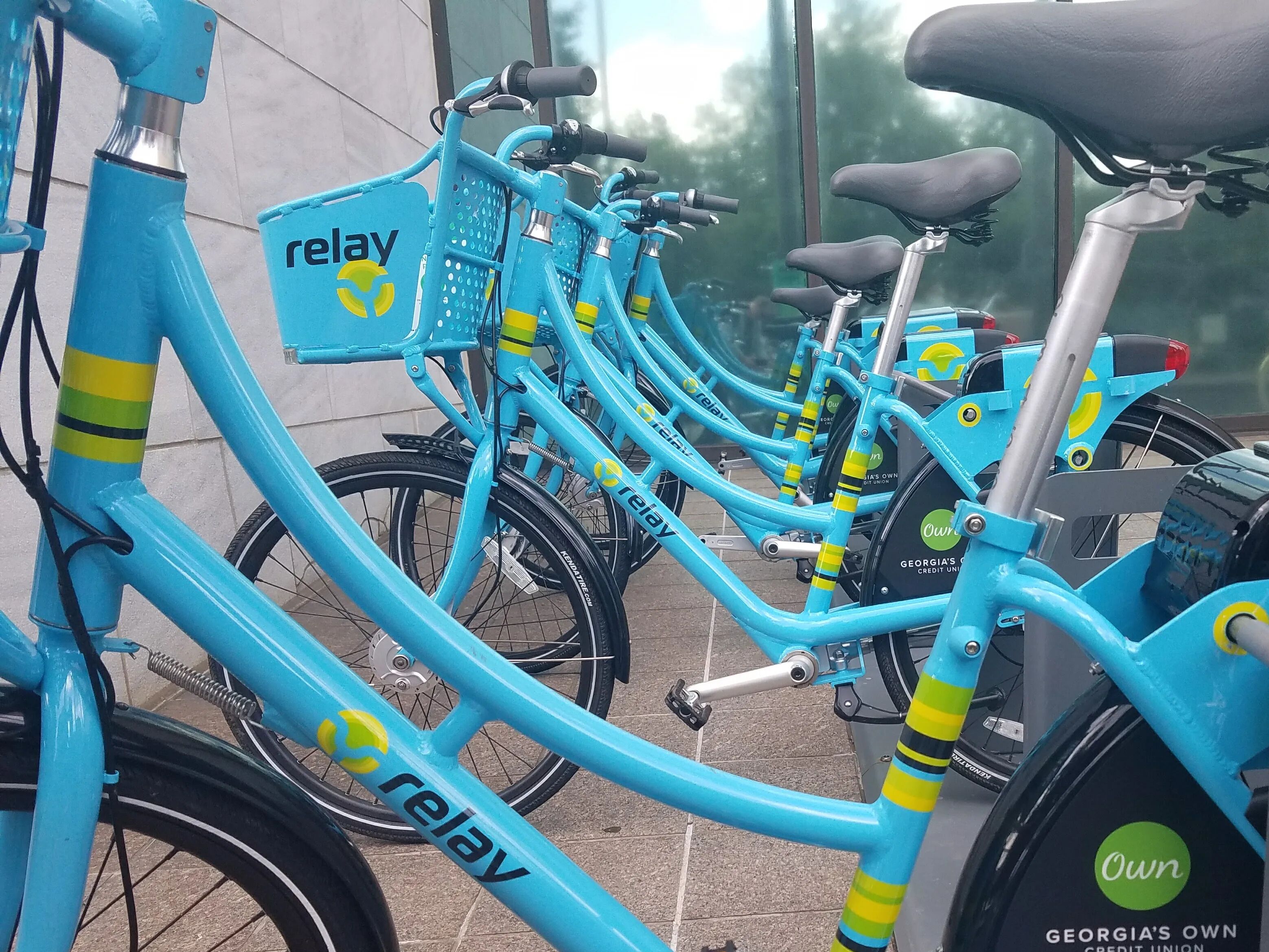 A row of blue bicycles with 'relay' branding, parked in an outdoor area with a tiled floor.
