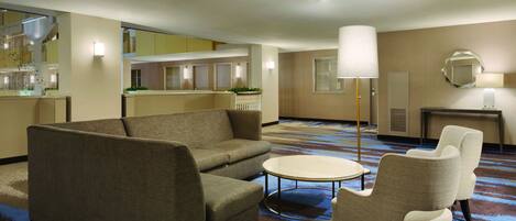 A hotel room with a sofa, armchairs, a small table, a lamp, and a mirror on the wall.