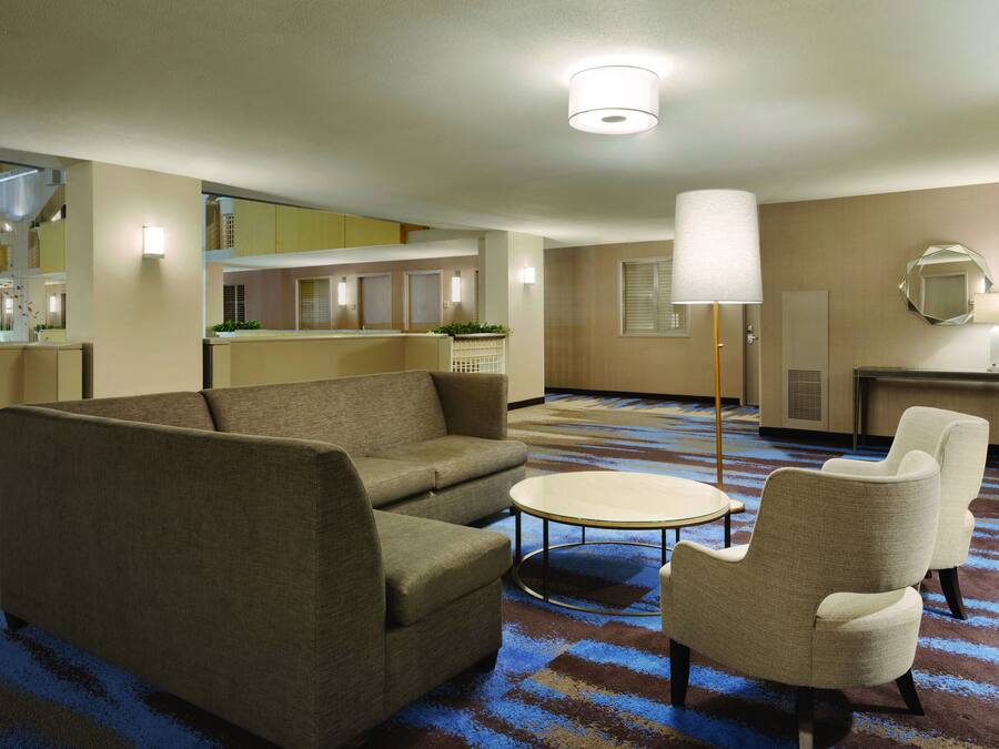 Een hotelkamer met een bank, fauteuils, een bijzettafeltje, een lamp en een spiegel aan de muur.