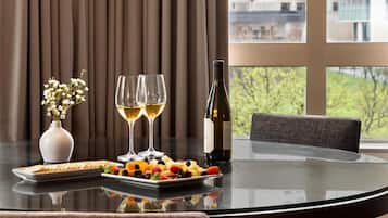 A table set with a bottle of wine, two glasses of white wine, a plate of assorted fruits, and a vase with flowers.