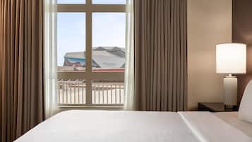 Una habitación de hotel con una cama grande, una mesita de noche con lámpara y una ventana con cortinas.