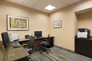 A hotel office with two desks, computers, printers, and framed artwork on the walls.
