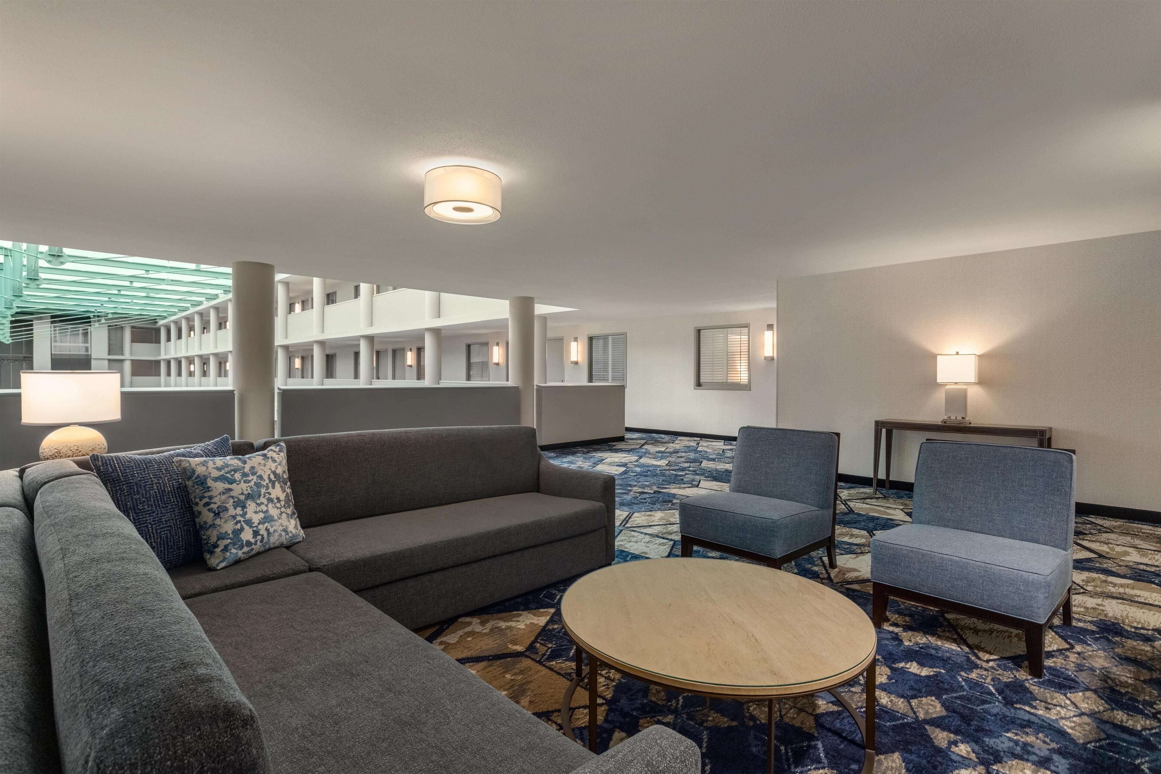 A hotel room with a sofa, chairs, a round table, and a patterned carpet.