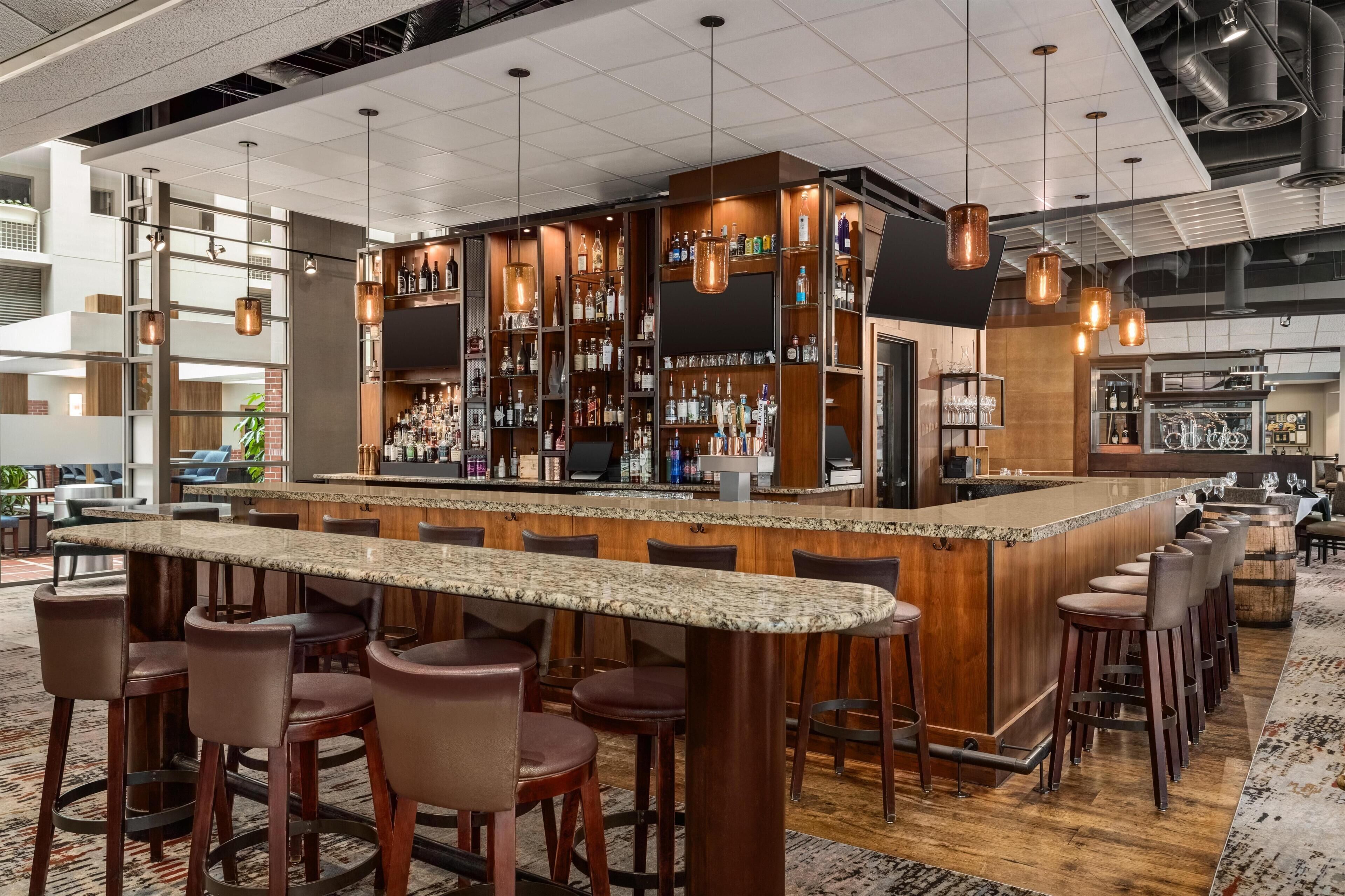 A bar area with a granite countertop, multiple stools, and a variety of bottles and glasses on shelves.