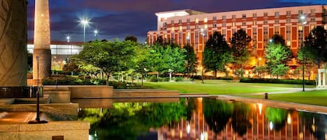 A hotel with a reflective pool, a well-lit building, and a landscaped garden.
