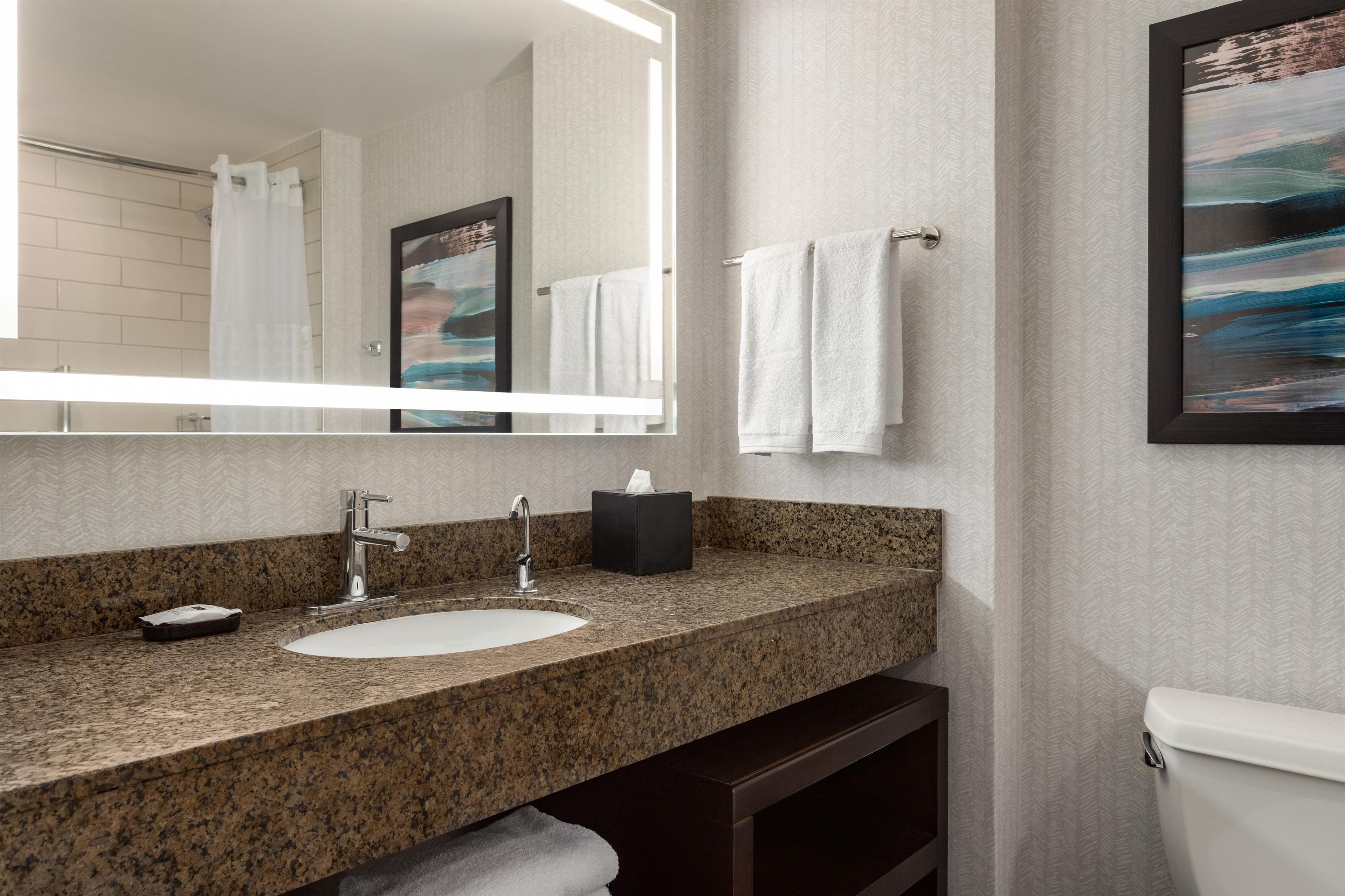 Un baño con encimera de granito, un lavabo blanco, un espejo y un perchero para toallas.