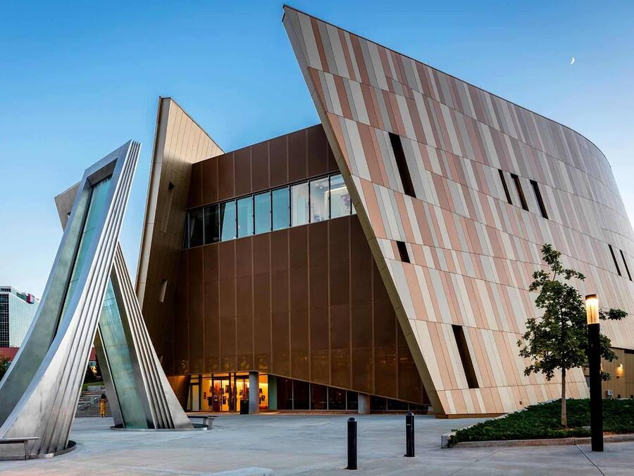 Ein modernes Gebäude mit einem markanten, winkligen Design, gekennzeichnet durch ein auffälliges Pultdach und eine große Glasfassade.
