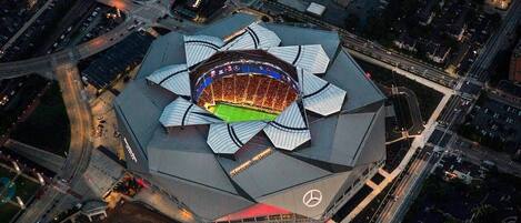 Vista aérea de un estadio con una estructura de techo distintiva en forma de flor, rodeado de calles y áreas de estacionamiento.