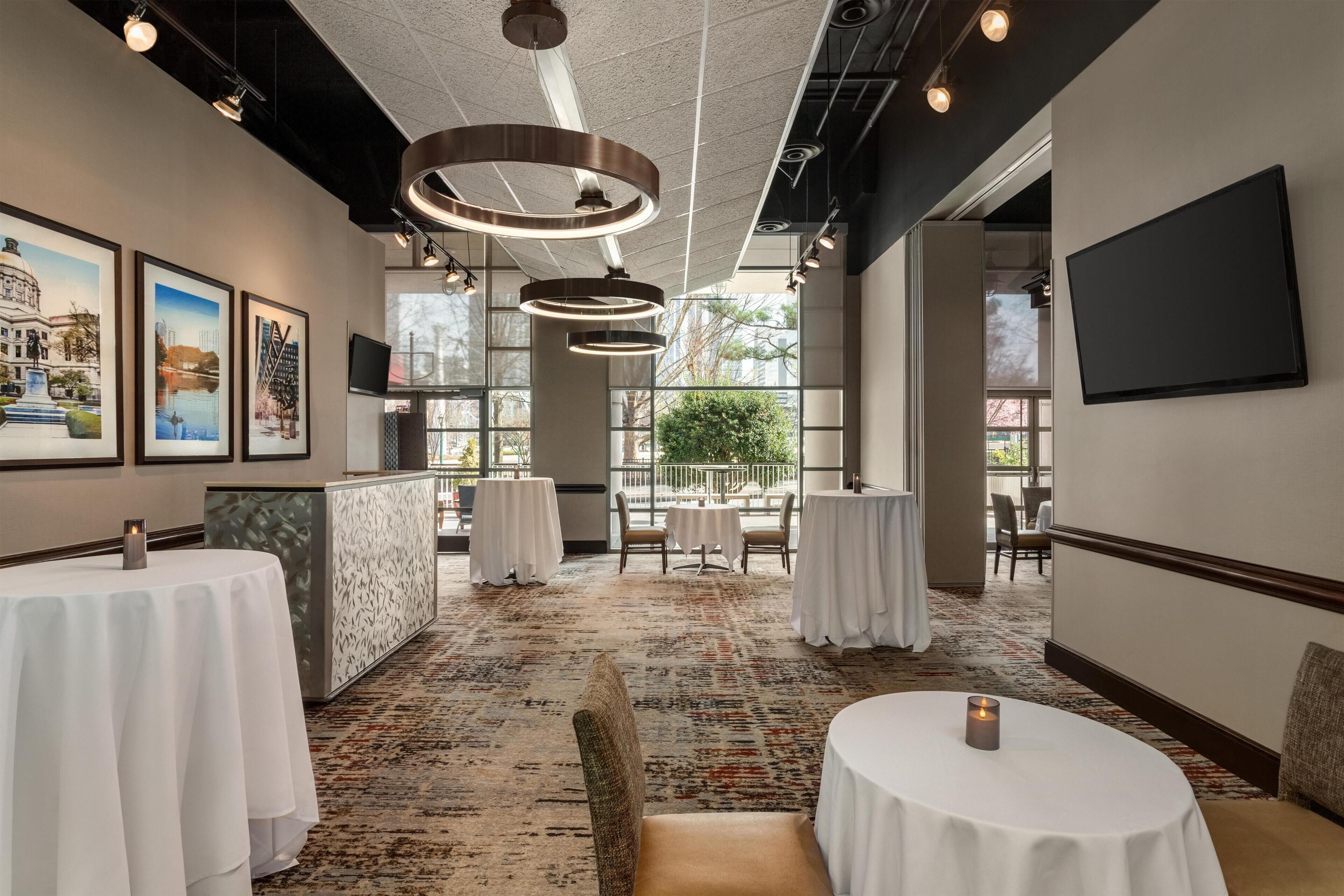 A hotel lobby with round tables, a reception desk, and framed pictures on the wall.