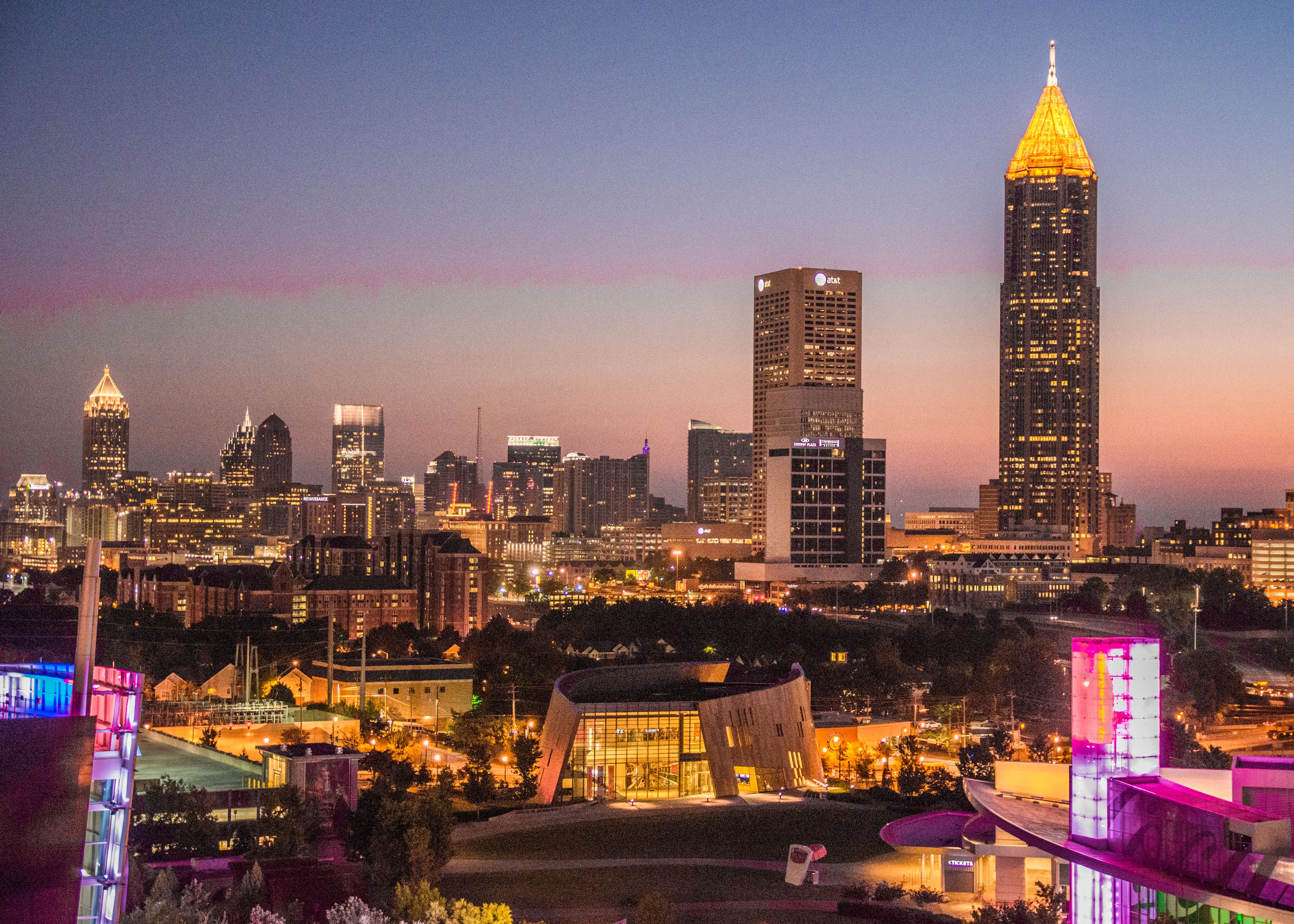 A city skyline at dusk with illuminated buildings and a prominent skyscraper.